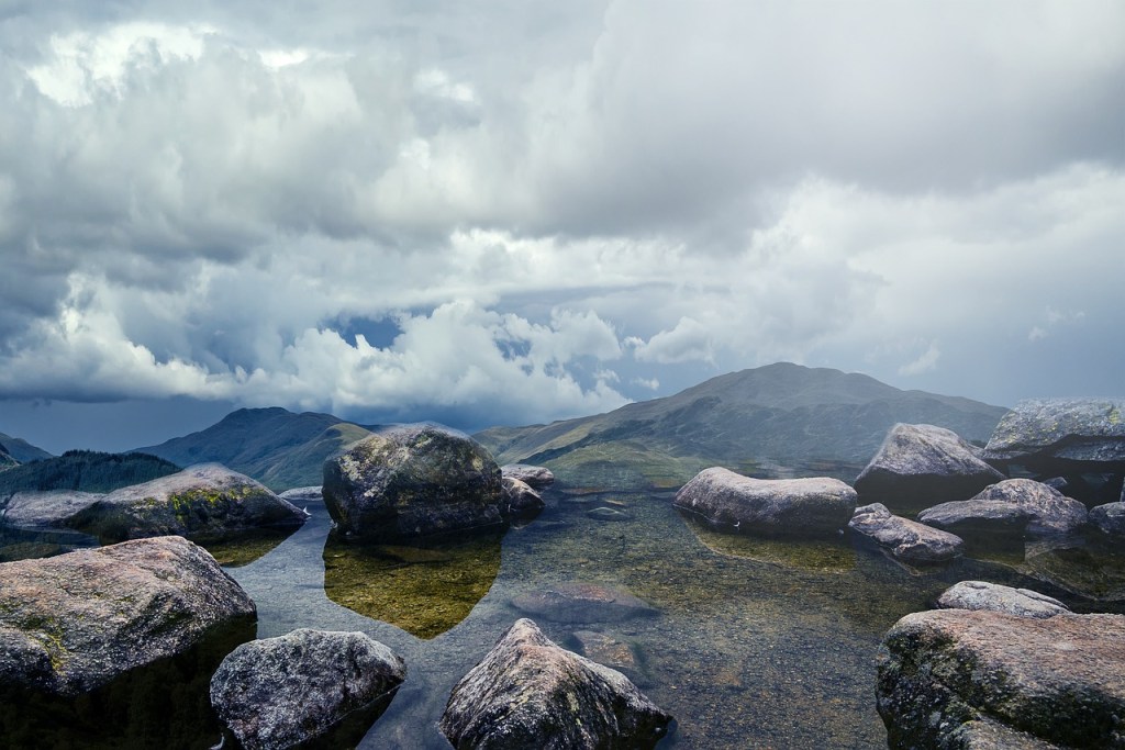 Clear water and rocks in lucid dream and sky with clouds and mountains on the background.